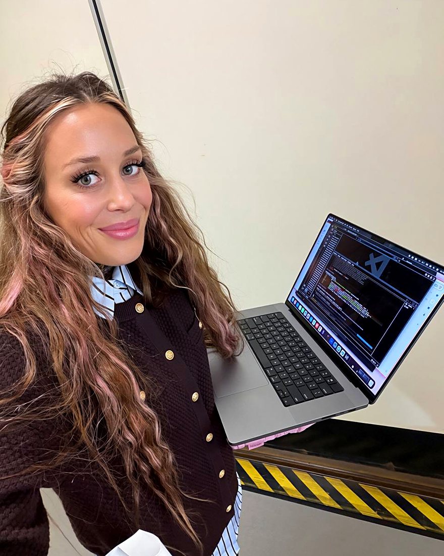 Amy with pink-streaked hair holding a laptop with code on the screen