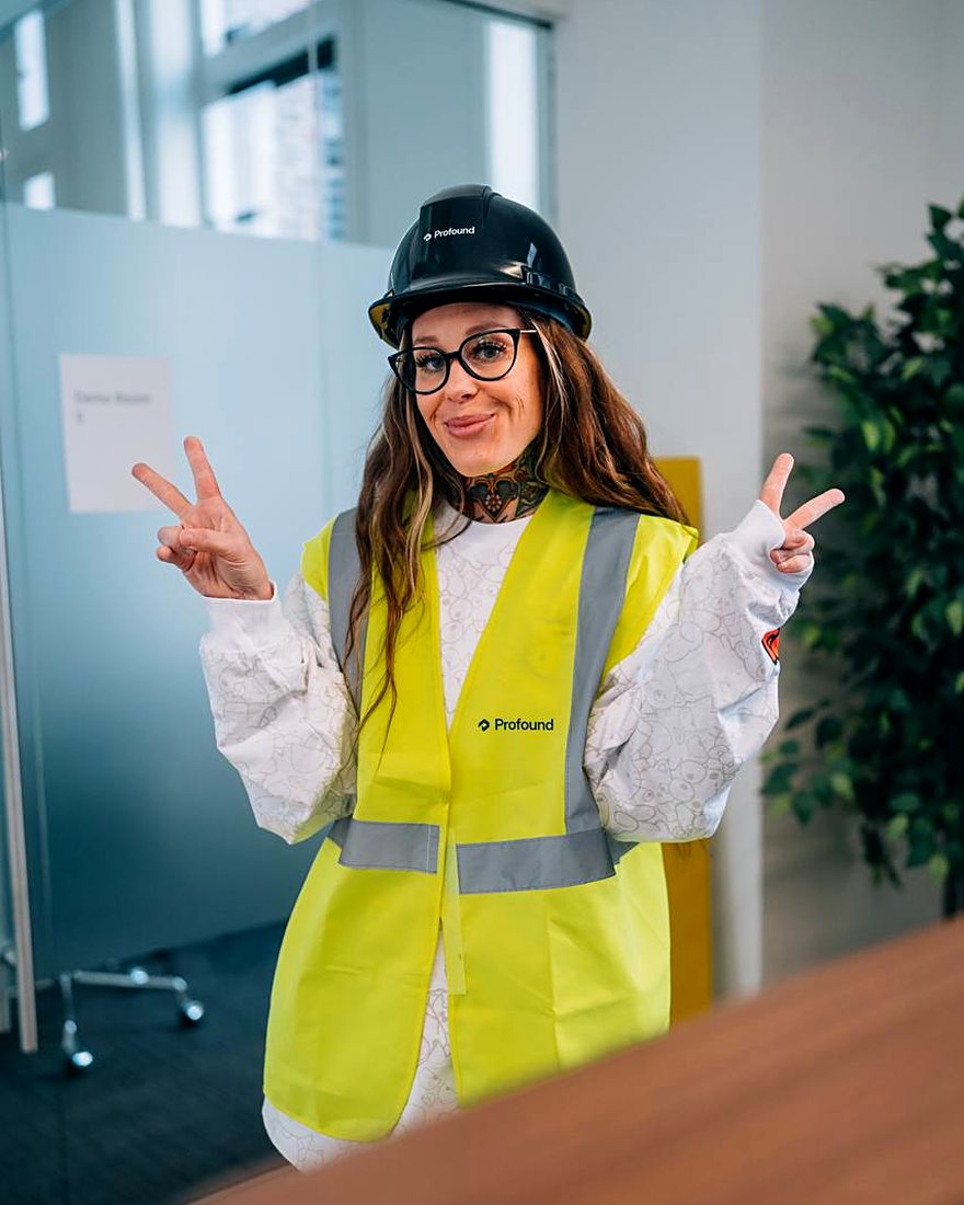 Amy in a hard hat and hi-vis vest over a Hello Kitty print shirt, throwing peace signs